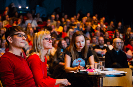 Publikum i Wergelandssalen med frivillig Andy Bennett, festivalsjef Kjersti Helgeland og medarrangør Marianne Støle-Nilsen i forgrunnen